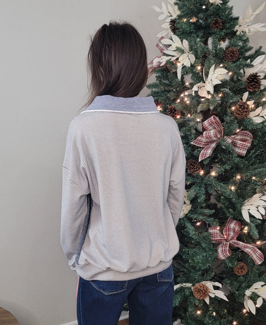 A person with long brown hair, wearing the Hem & Thread Shay Striped Mix Pullover and jeans, stands with their back to the camera in front of a decorated Christmas tree adorned with lights, pine cones, and plaid ribbon bows.
