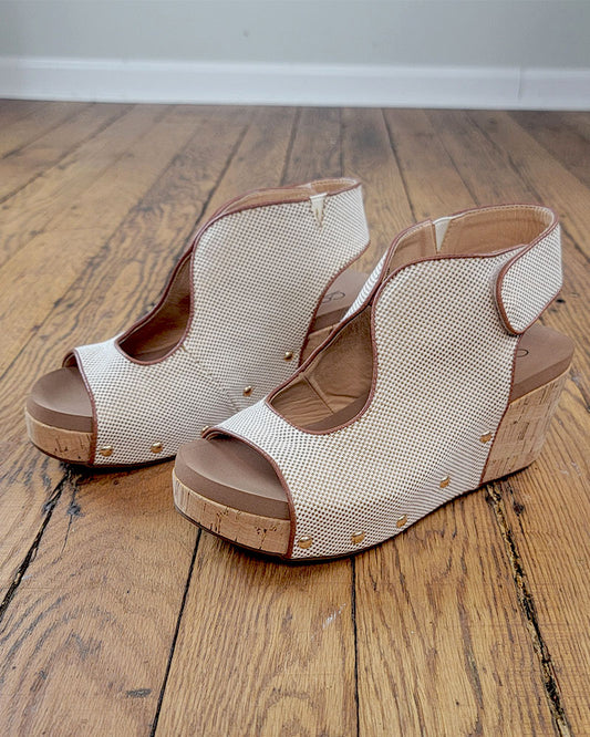 The Frisky Sandal from Corkys features beige textured uppers, open toes, and cork wedge heels, shown on a wooden floor against a plain white wall.