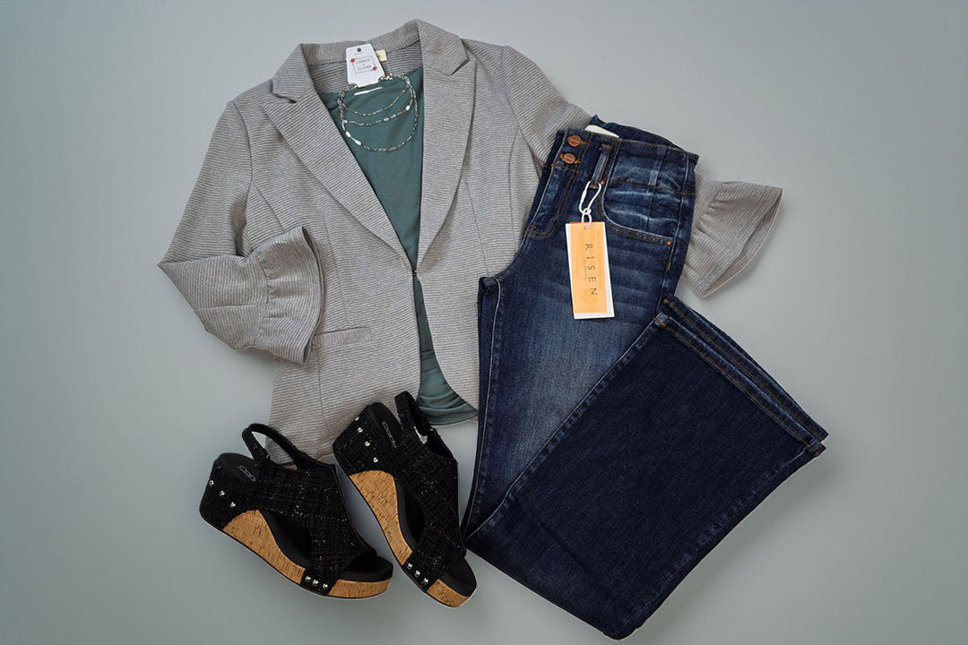 Gray blazer, teal top, dark jeans and black wedges flat lay on blue/gray background
