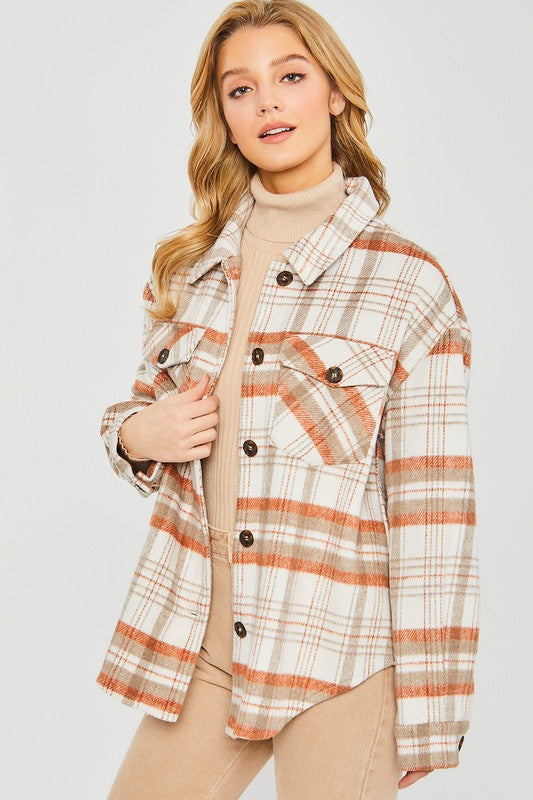 A young woman with long blonde hair wears the Love Tree Plaid Bust Pocket Shacket in white, beige, and orange over a beige turtleneck sweater and tan pants, standing against a plain light background.