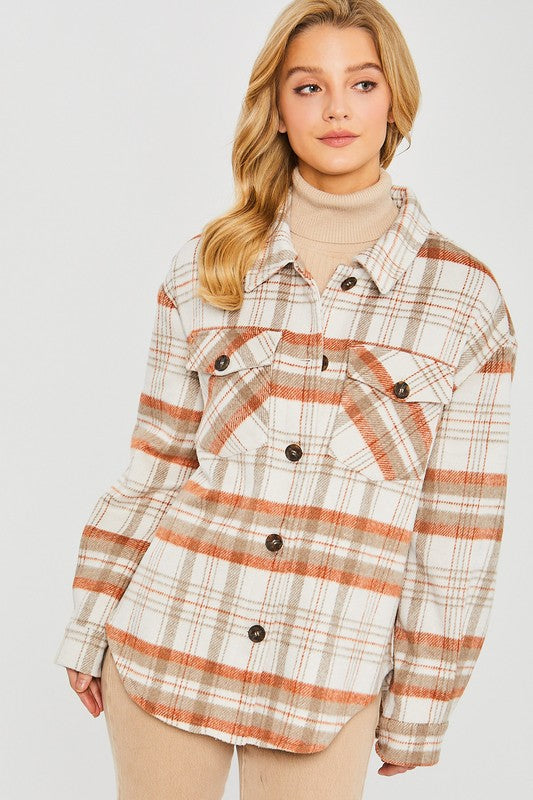 A young woman with long blonde hair wears the Love Tree Plaid Bust Pocket Shacket in cream, brown, and rust over a beige turtleneck. She stands against a plain light background, looking slightly to the side.