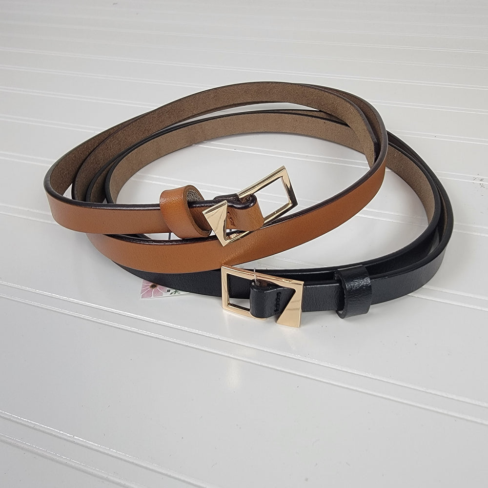 Two Asymmetrical Buckle Skinny Belts from Leto Collection, one brown and one black, are coiled together on a white ridged surface, each showcasing a distinctive gold buckle design.