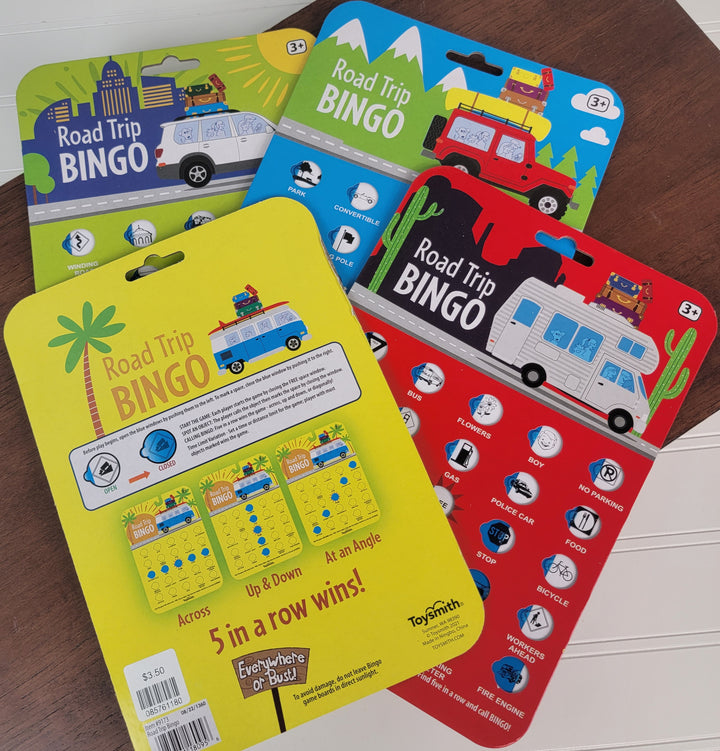 Four reusable Road Trip Travel BINGO cards by Toysmith, each with travel-themed illustrations and vehicle images, are displayed on a wooden surface—perfect for fun games on the go.