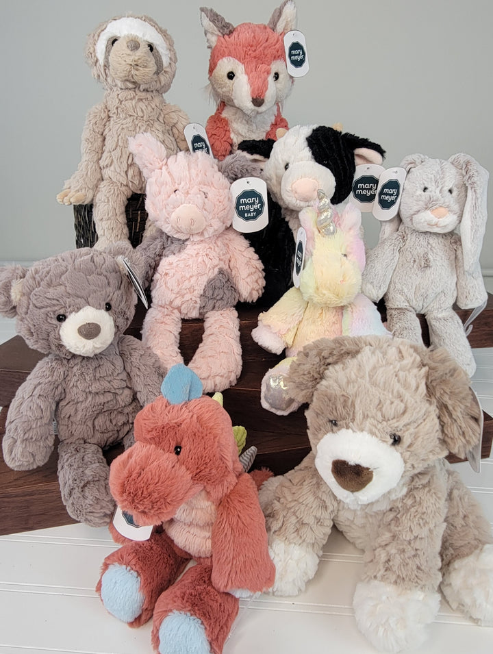 The Mary Meyer Kids Plush Animals set features nine adorable plushies, including a sloth, fox, two bunnies, cow, unicorn, bear, dinosaur, and dog—perfect for kids and displayed on wooden steps against a neutral background.