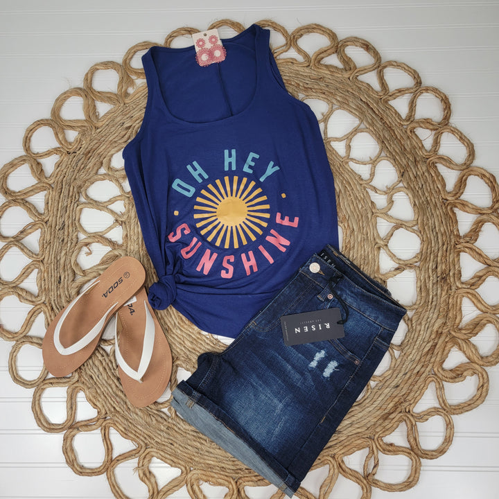 The Zenana "Oh Hey Sunshine" Tank features a blue graphic design with sun motif, styled with dark denim shorts and tan sandals for a flattering look, all arranged on a round woven mat.