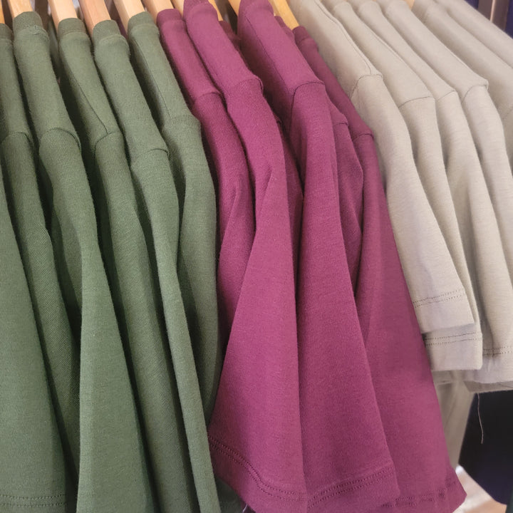 Zenana Basic Tee short sleeve round neck t-shirts in green, purple, and beige hang on wooden hangers in a row—ideal for comfy layering.