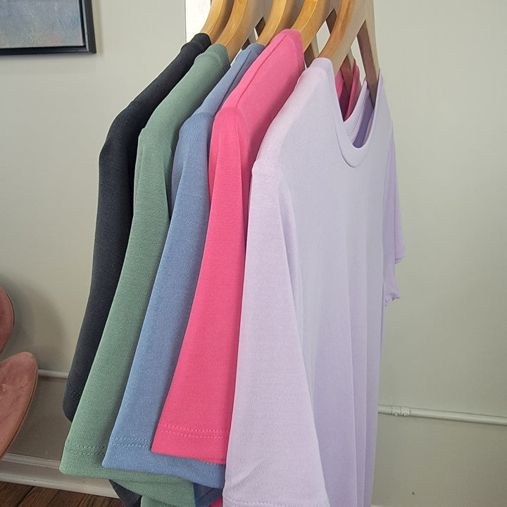 Five Keely Tees by HYFVE, Inc in black, green, blue, pink, and light purple hang on wooden hangers against a light-colored wall.