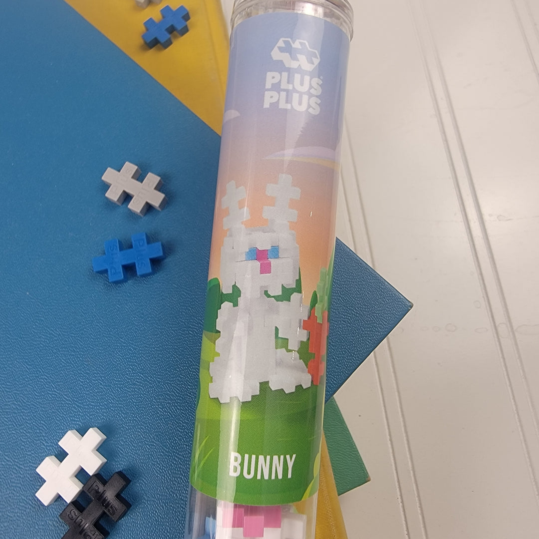 The Plus Plus Puzzle Tubes by Plus Plus show a white bunny built from blue, white, and black pieces, with extra parts scattered on colored paper nearby.