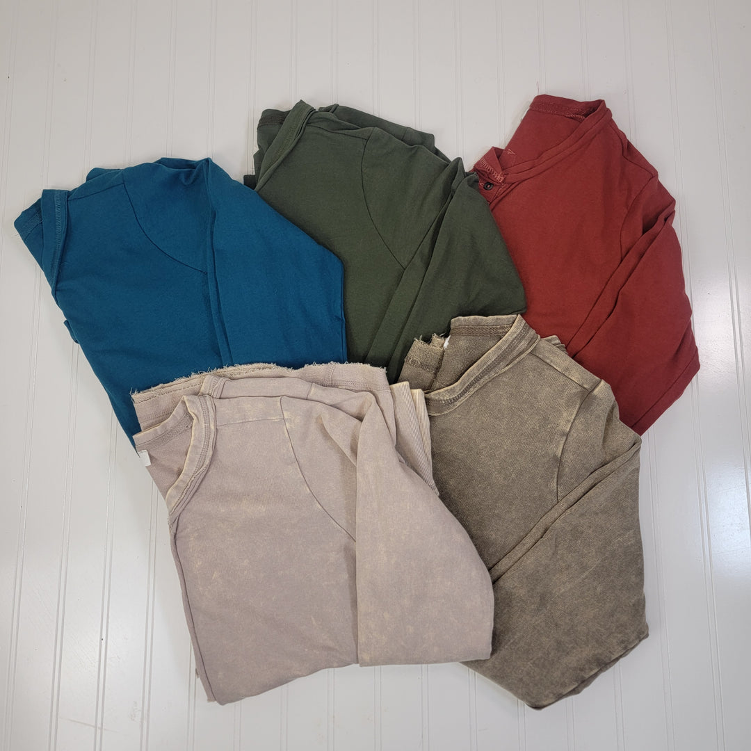 Five ZENANA Della Long Sleeve Tops in teal, green, red, beige, and brown are folded in a circle on a white wood background.