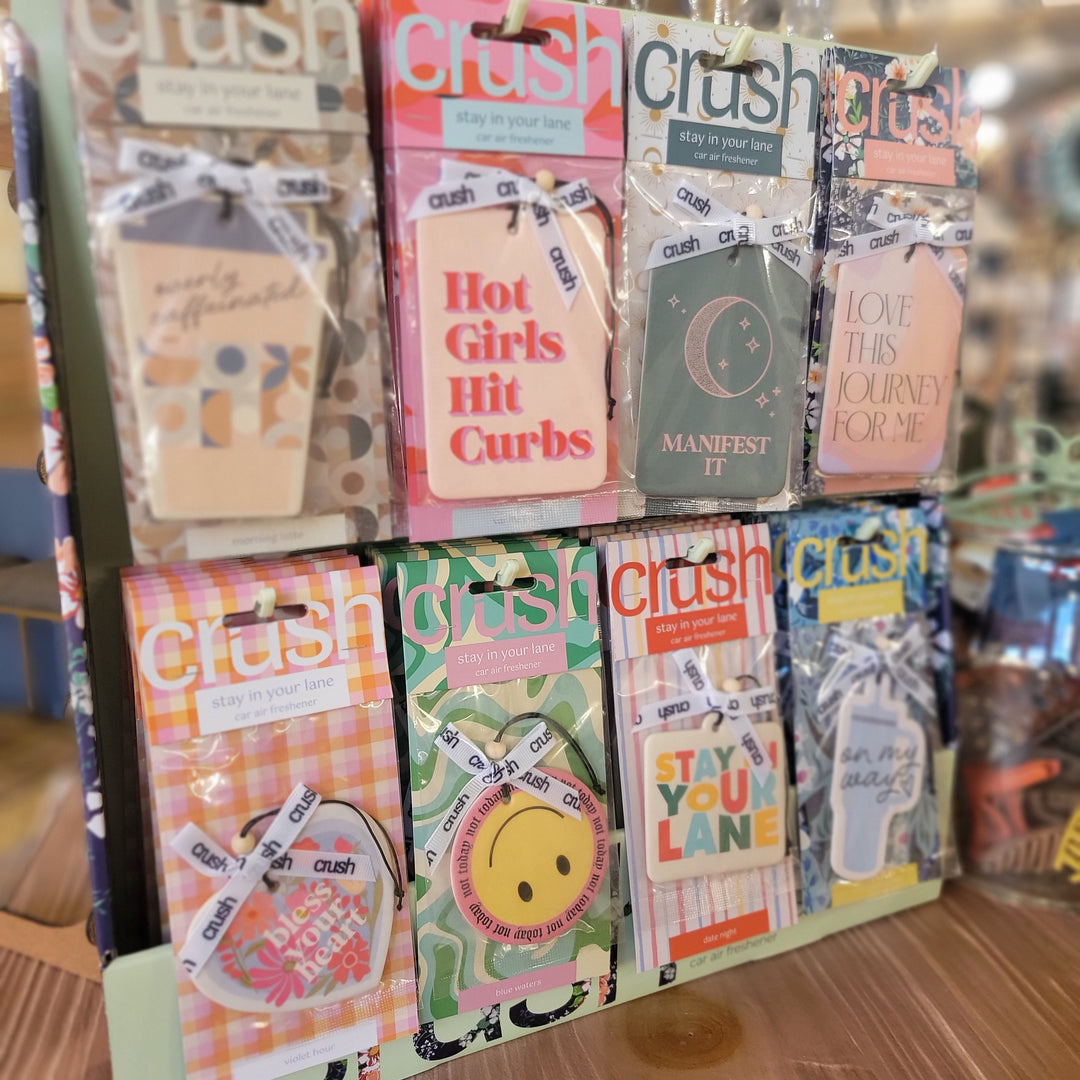 DM Merchandising Air Freshners come in a display stand with three rows of colorful, fun designs and phrases like “Hot Girls Hit Curbs,” “Manifest It,” and “Stay in Your Lane”—perfect as cool car or gift air fresheners.