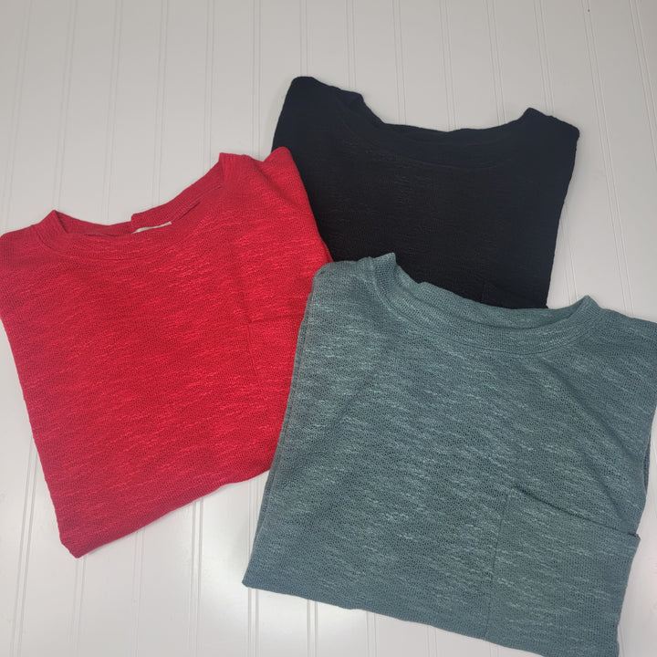 Three Catalina Long Sleeve Tops by ZENANA, in red, black, and teal soft slub hacci fabric, are neatly folded on a white textured surface. Each crew neck features a visible chest pocket.