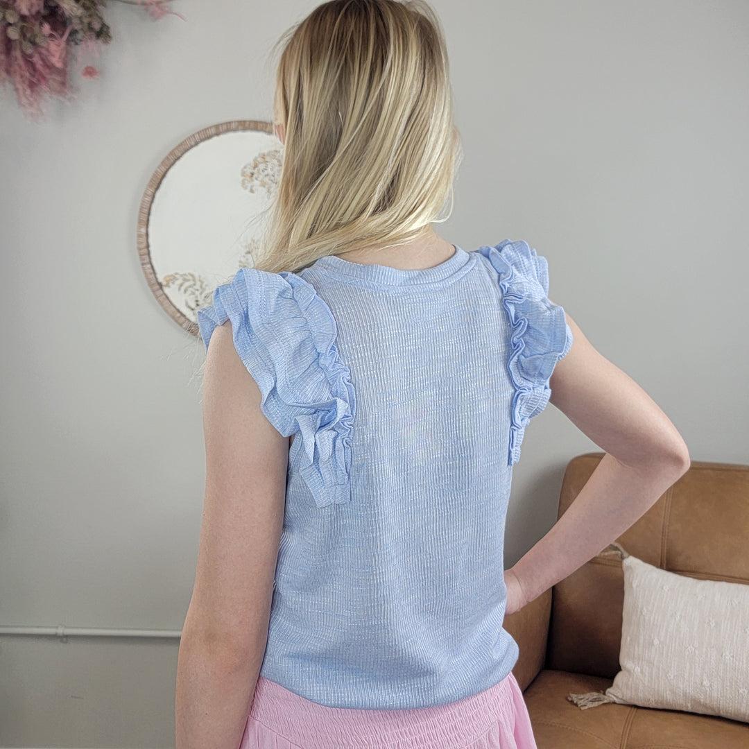 A girl in the Hayden Girls Jemma Top, featuring an ice blue ruffle design.