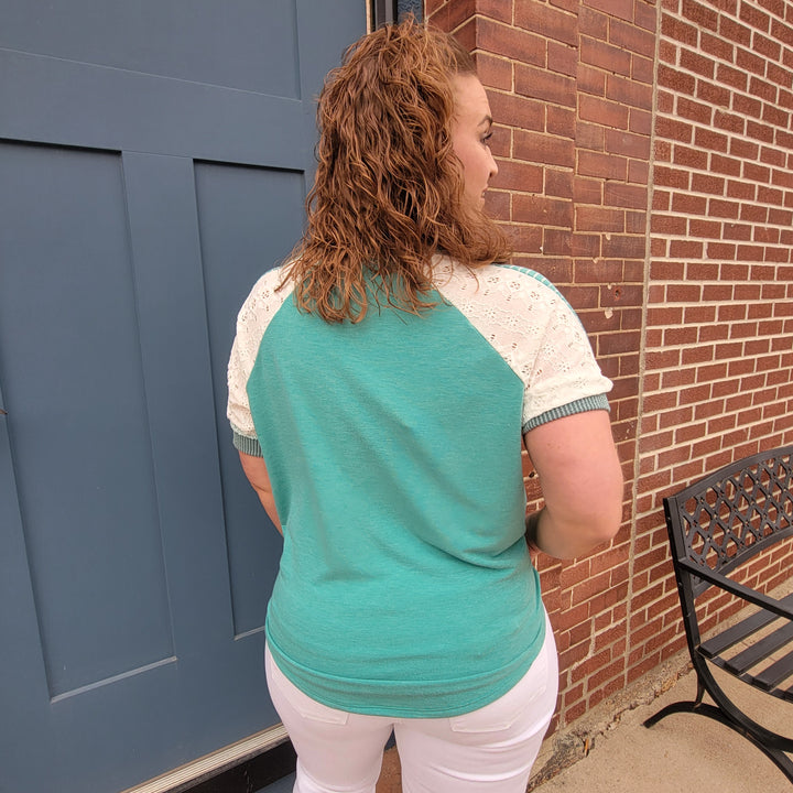 A woman in a 7th Ray Lainey Patchwork V-Neck Top stands in front of a brick building.