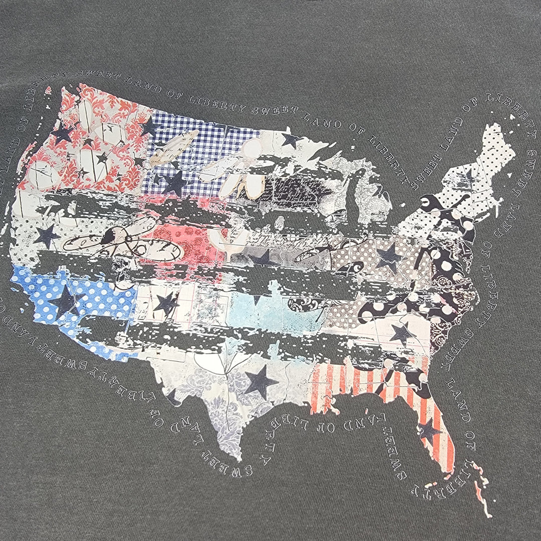 The Distressed USA Tee by Cosmos + Clover Boutique features a USA map with stripes, stars, florals, and checks on a gray 100% cotton Comfort Colors shirt. Surrounding text fades around the design for a unique look.