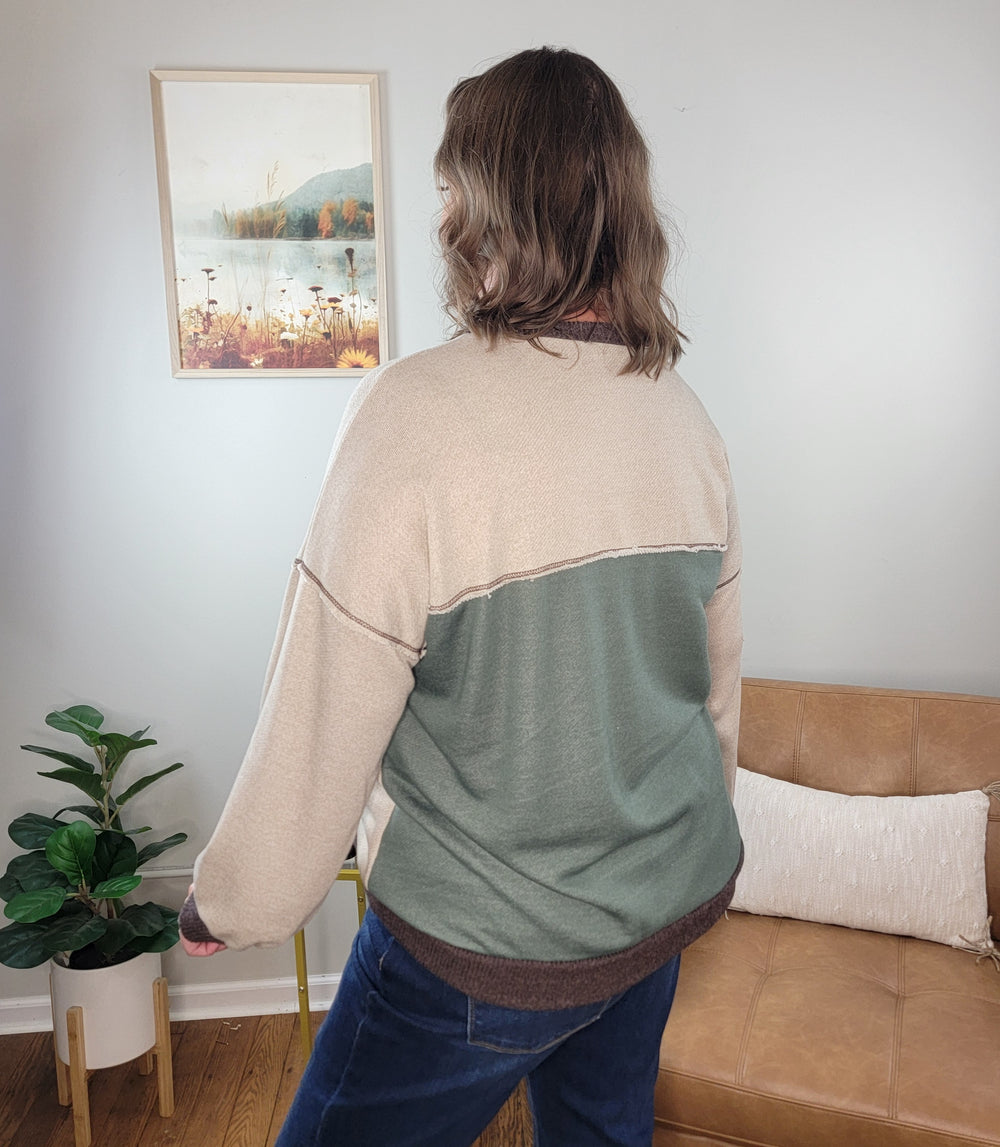 Back view of a person wearing a Lovely Melody Michelle Color Block Knit Sweatshirt featuring a beige upper section, a sage green lower section, and dark brown trim at the neckline and hem.