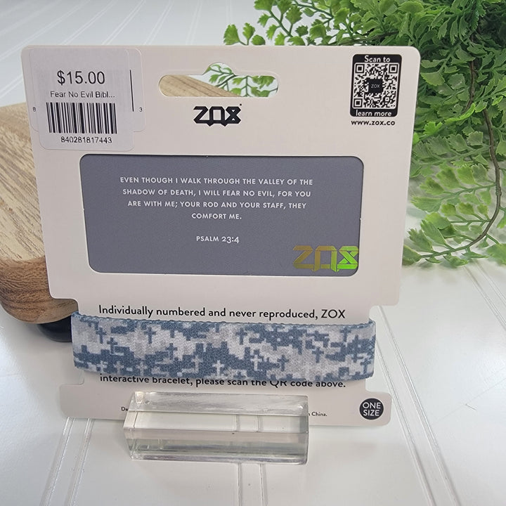 A blue and white digital camo-patterned ZOX Bracelet by ZOX, made from recycled water bottles, is shown on packaging with Psalm 23:4 and a $15 price tag. Blurred green plants appear in the background.