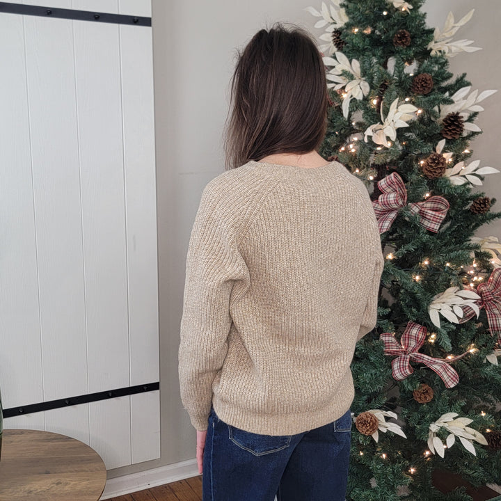 A person with long brown hair, wearing the Hem &amp; Thread Alayla Tie Neck Knit Sweater and blue jeans, stands with their back to the camera by a Christmas tree decorated with lights, bows, and white ornaments.