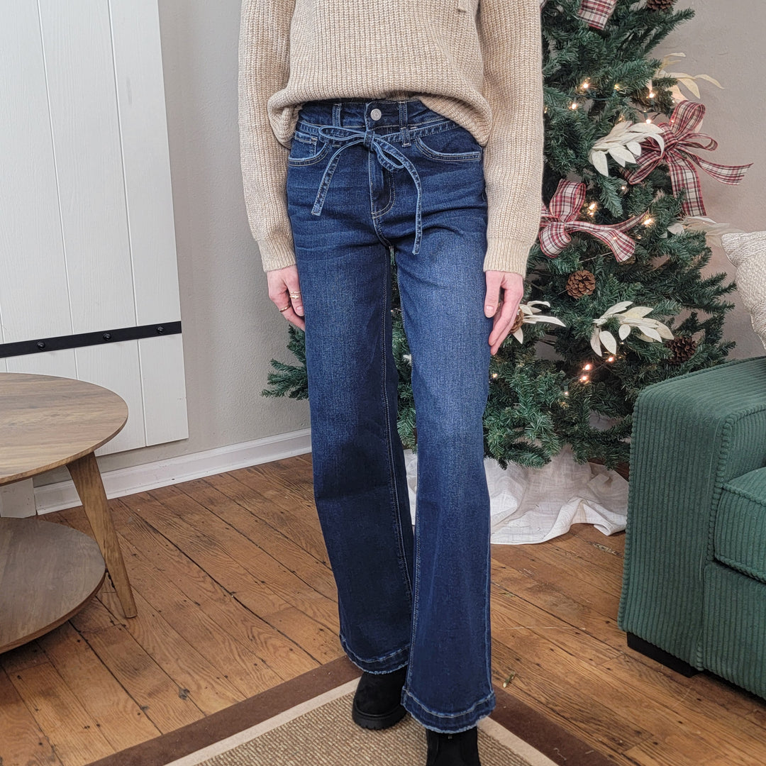 Person wearing Risen brand blue jeans standing in front of a decorated Christmas tree. Wide leg jeans with tie waist.