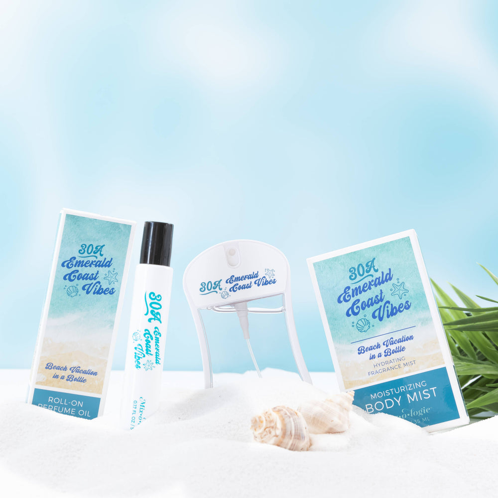Mixologie’s 30A Emerald Coast Vibes Moisturizing Body Mist is displayed on white sand with seashells, tropical leaves, and a clear blue sky, evoking a fresh beach fragrance scene.