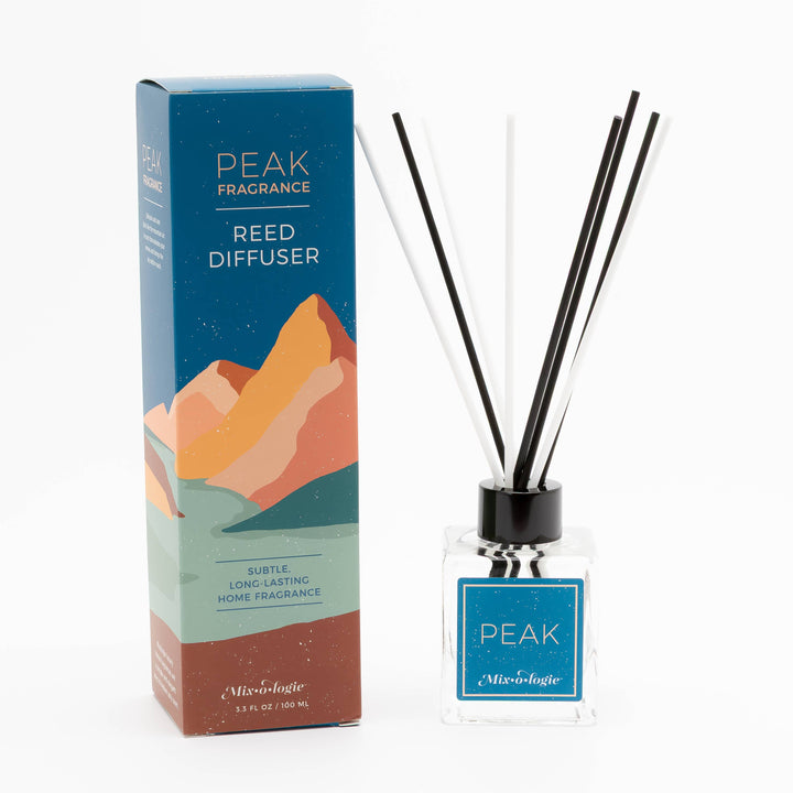 The Mixologie Peak | Reed Diffuser features black and white reeds in a clear glass bottle beside its mountain-artwork box, providing a subtle, long-lasting luxury home fragrance for an elegant, flameless aroma.