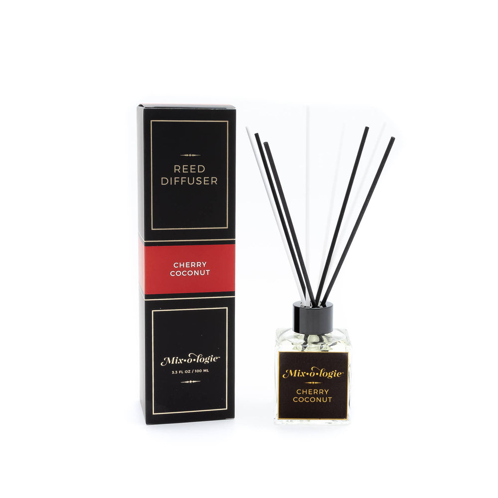 A boxed Mixologie Reed Diffuser in Cherry Coconut stands with a glass bottle and black reeds—both featuring black and gold accents—making Reed Diffusers from Mixologie an elegant hostess gift.