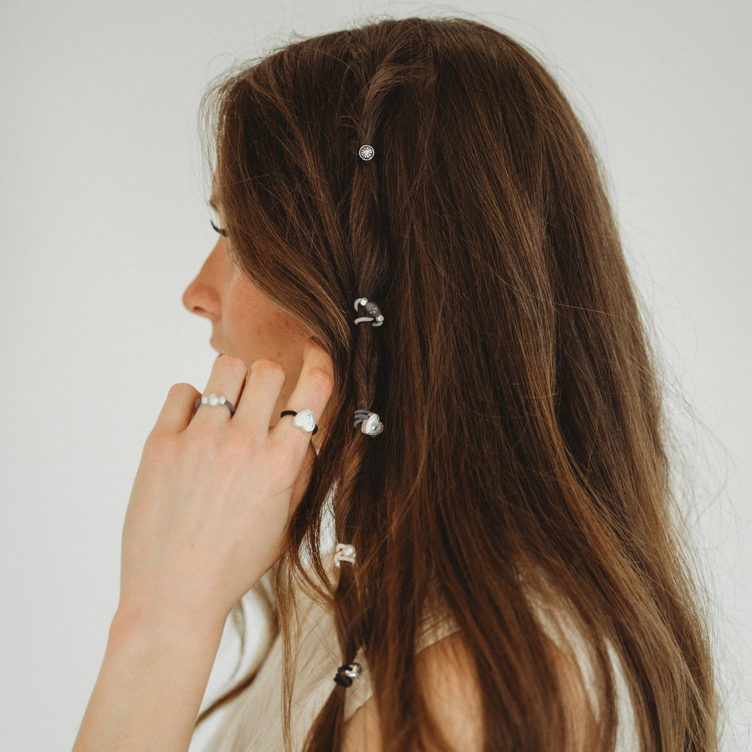 A person with long brown hair wears K’lani “Luna” Silver &amp; Cool Tones Hair Tie Rings as silver accents, along with delicate pearl hair accessories braided into their hair for an elegant touch. The photo is taken from the side against a plain background.