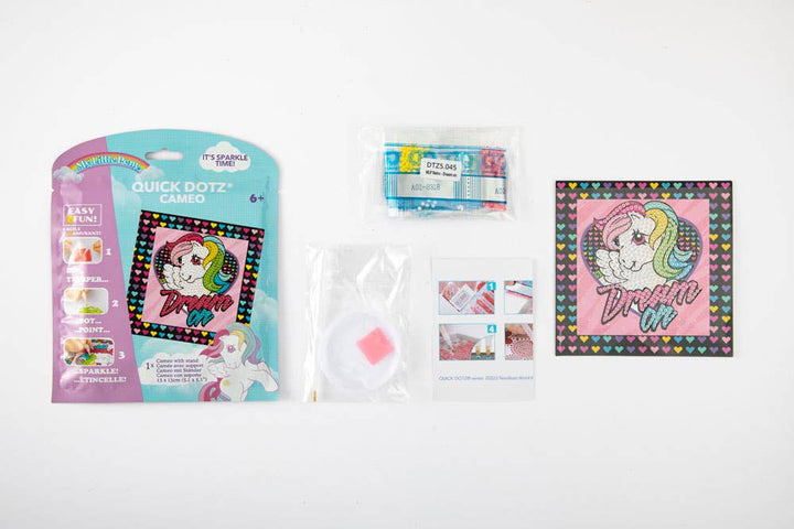The Toysmith Diamond Dotz MLP Retro - Dream On kit includes packaging, diamond beads, crafting tools, instructions, and a finished square unicorn artwork on a pink and black heart-patterned background with "Dream On" text.