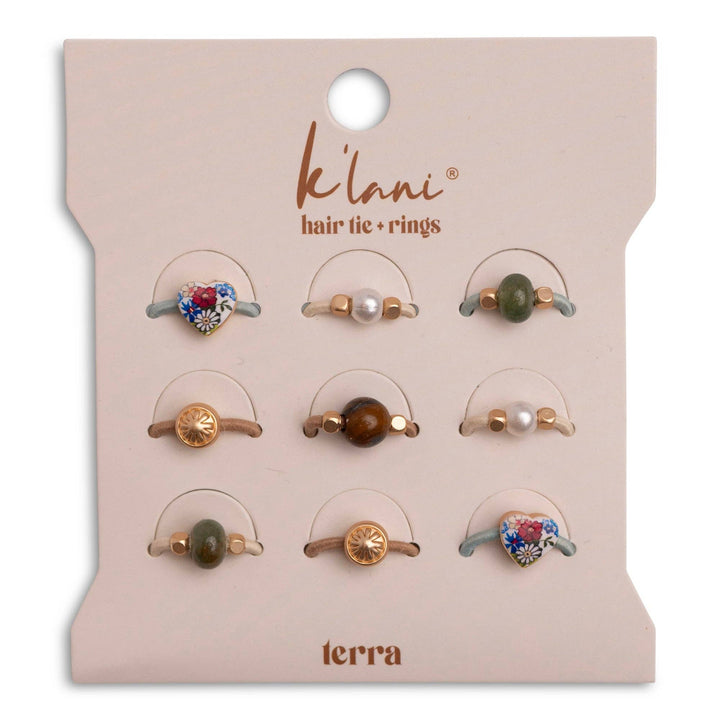 A set of nine versatile and decorative hair accessories—hair ties and hair tie rings—from K’lani hair tie bracelets, displayed on a beige card labeled “Terra” Earth Tones Hair Tie Rings. The collection features playful designs with hearts, pearls, beads, and gold accents.