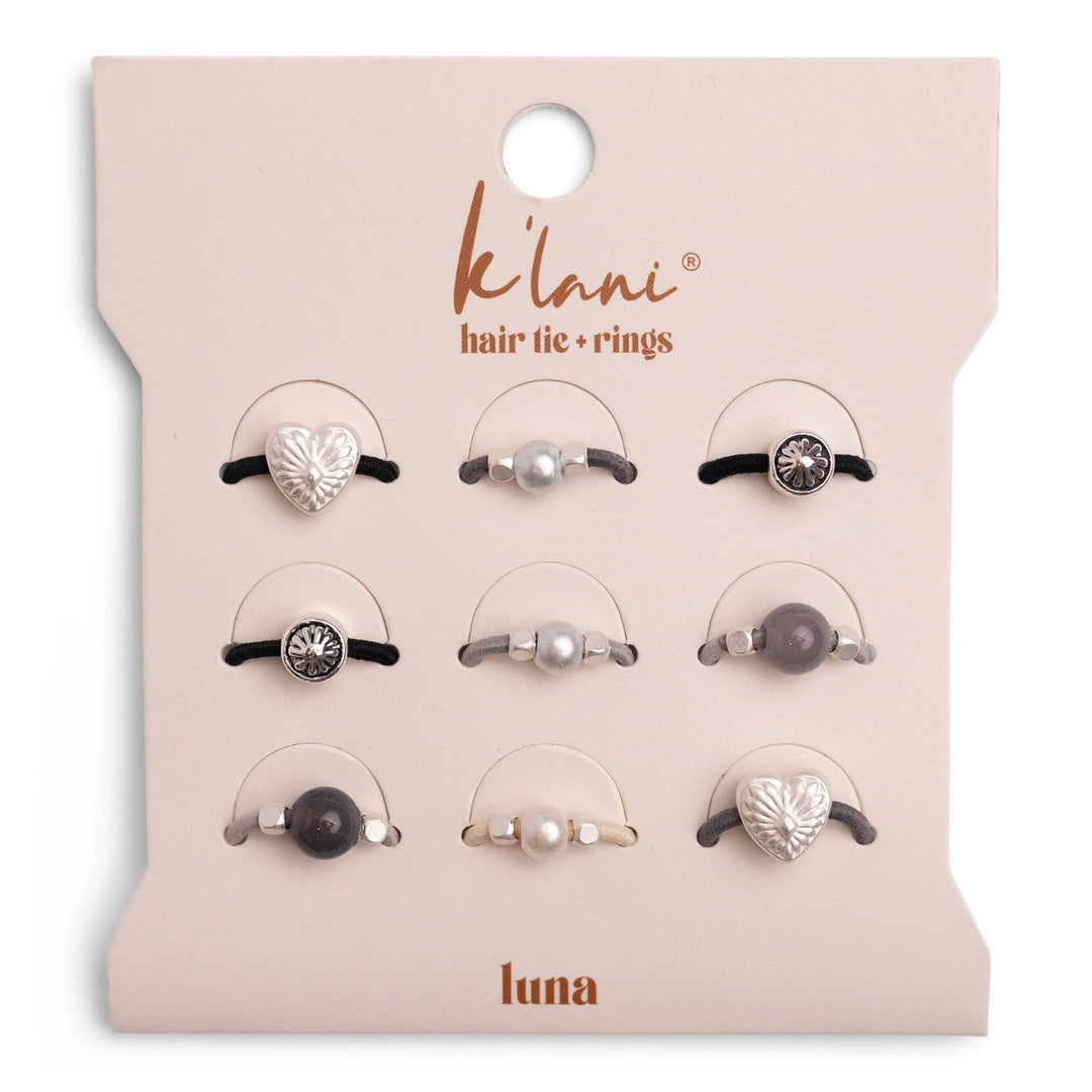 A set of nine stretchy hair ties with attached rings in heart, pearl, and gemstone designs, from the K’lani hair tie bracelets “Luna” Silver & Cool Tones Hair Tie Rings collection, displayed on a branded card.