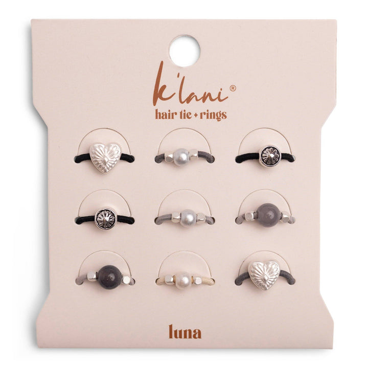 A set of nine stretchy hair ties with attached rings in heart, pearl, and gemstone designs, from the K’lani hair tie bracelets “Luna” Silver &amp; Cool Tones Hair Tie Rings collection, displayed on a branded card.