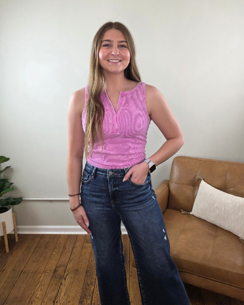 Woman wearing the Anja ribbed Henley tank in mauve along with dark wash, wide leg jeans, standing in a living room. 