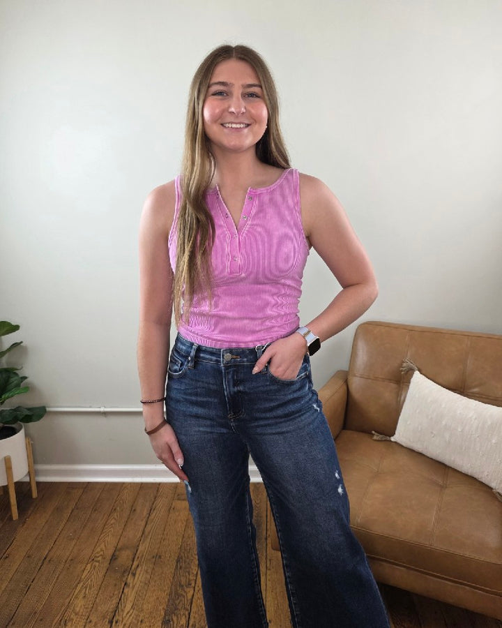 Woman wearing the Anja ribbed Henley tank in mauve along with dark wash, wide leg jeans, standing in a living room. 