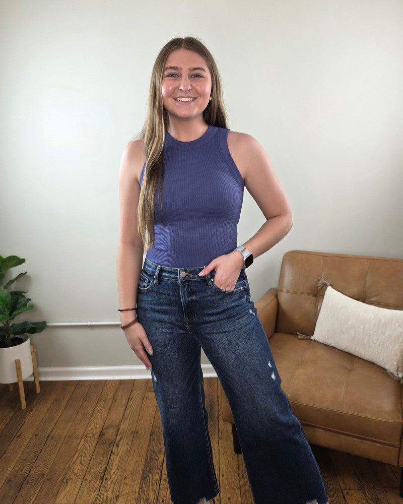 Woman standing in a living room wearing the Burke cropped tank top in the color Marlin and wide leg, dark wash jeans. 