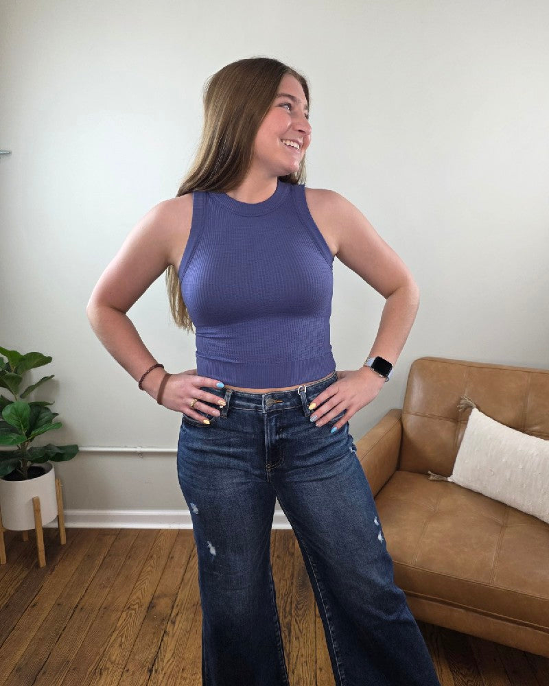 Woman standing in a living room wearing the Burke cropped tank top in the color Marlin and wide leg, dark wash jeans. 