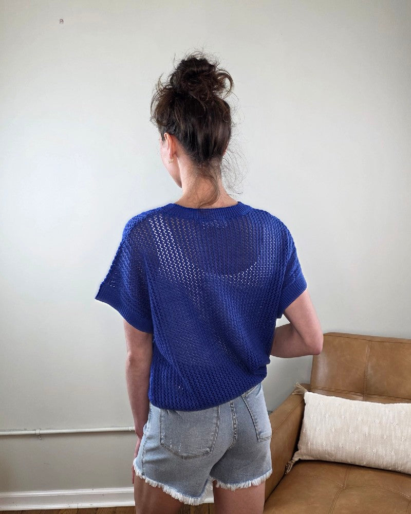 Woman wearing the Camille Open Knit Short sleeve Top a blue with denim shorts indoors.