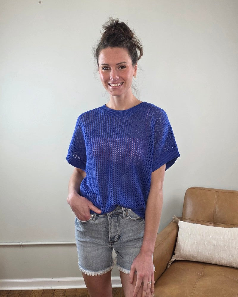 Woman wearing the Camille Open Knit Short sleeve Top a blue with denim shorts indoors.