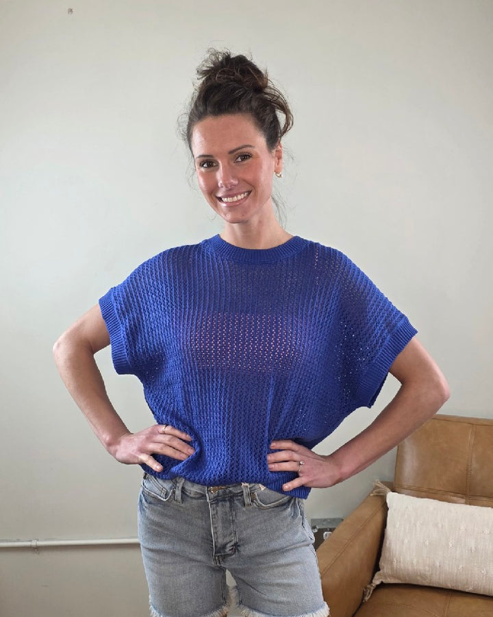 Woman wearing the Camille Open Knit Short sleeve Top a blue with denim shorts indoors.