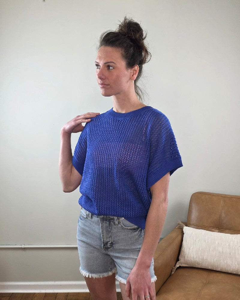 Woman wearing the Camille Open Knit Short sleeve Top a blue with denim shorts indoors.