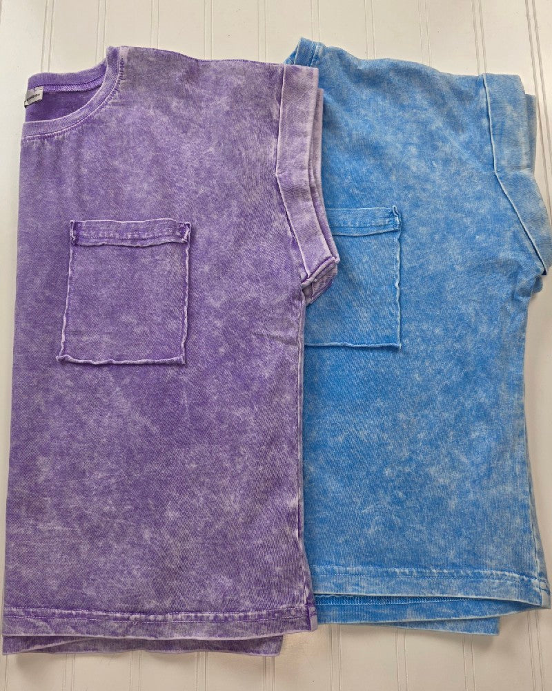 Two folded ZENANA Candace Snow Washed Cropped Short Sleeve Tops with chest pockets in faded purple and blue lie side by side on a white surface, showing off their textured cotton wash for relaxed summer style.