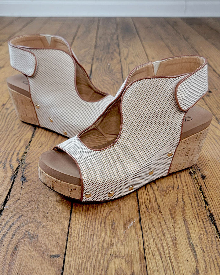 The Frisky Sandal from Corkys features beige mesh uppers, cork heels, and gold stud accents for a stylish look and comfort—shown here on a wooden floor.
