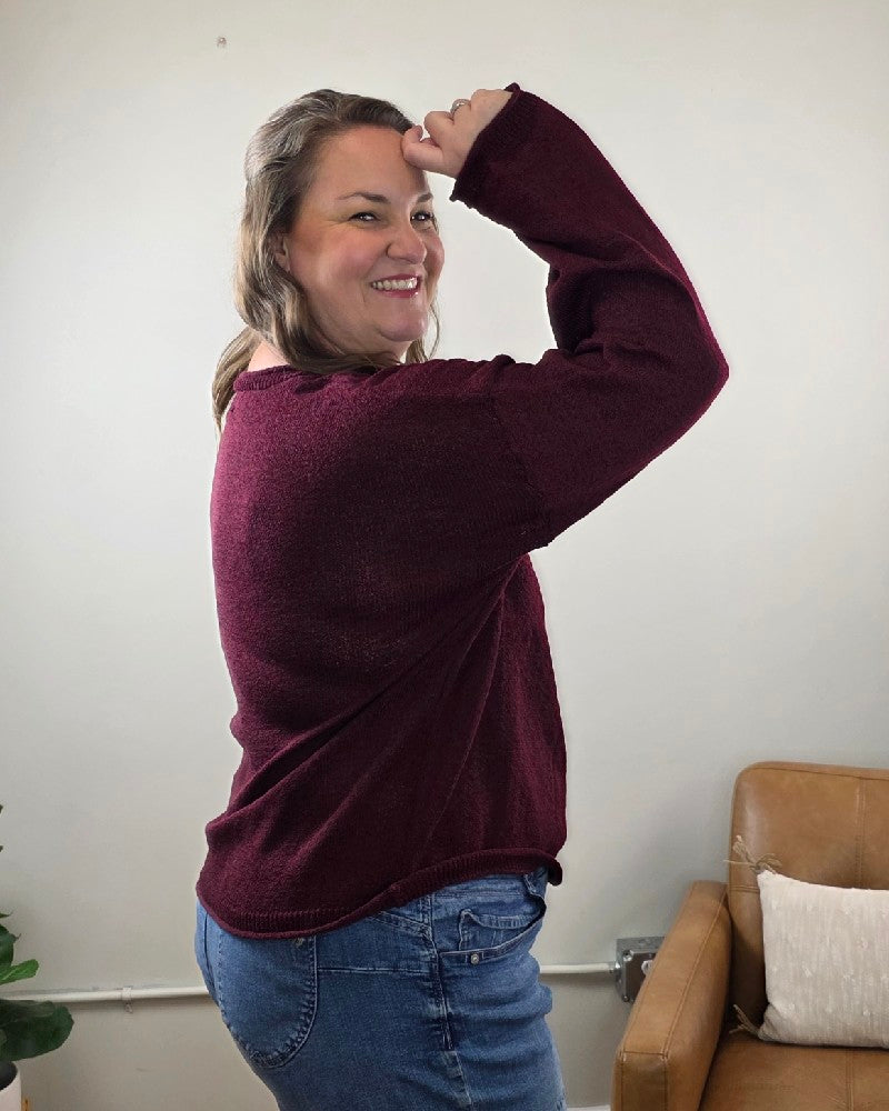 A woman wearing a maroon blu pepper Ella Long Sleeve Sweater in a stretchy knit with jeans, smiling over her shoulder.
