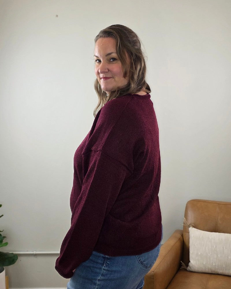 A woman wearing a maroon blu pepper Ella Long Sleeve Sweater and blue jeans, turned to look over her shoulder.