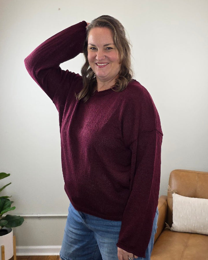 A woman smiling while wearing a long-sleeved, deep burgundy blu pepper Ella Long Sleeve Sweater and blue jeans.
