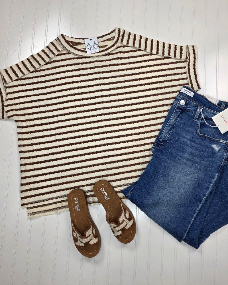 The ZENANA Esther Striped Short Sleeve Hi-low Tee in brown and cream is styled with blue jeans and brown sandals, all arranged on a white textured background.