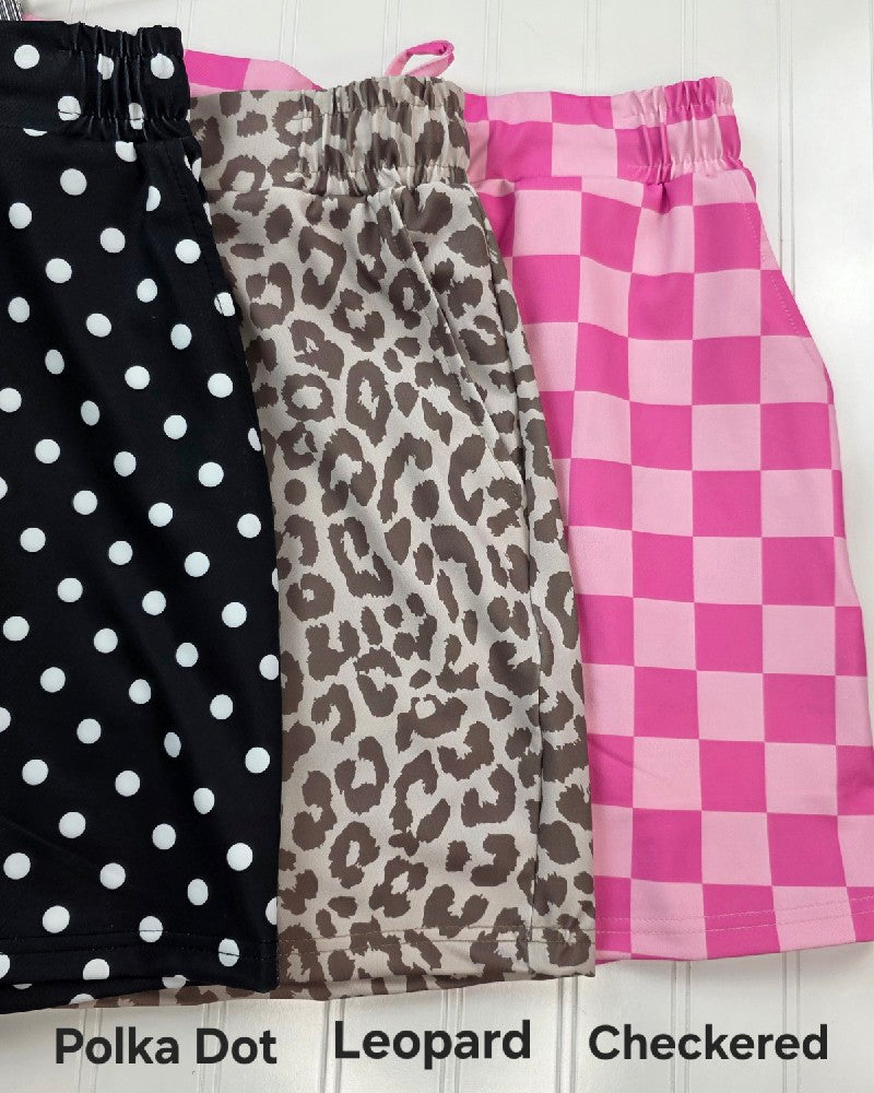 Three Jess Lea Everyday Skorts in stylish summer patterns—black and white polka dots, beige and brown leopard print, and pink checkered—are displayed side by side with labels identifying each versatile, comfy design.