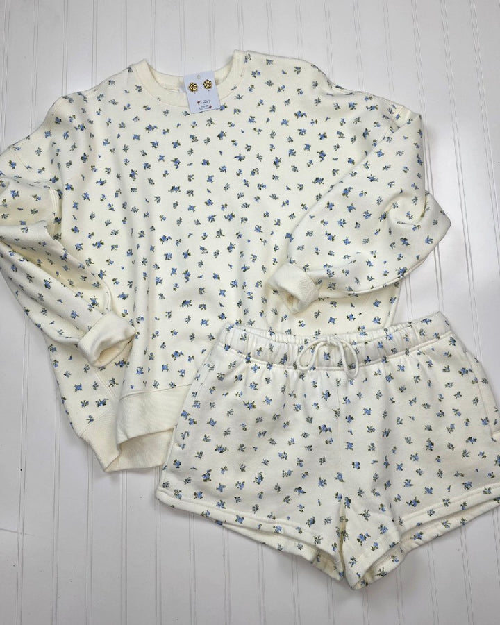 A soft cotton lounge set featuring HYFVE, Inc’s cream-colored long-sleeve top with Kalie Floral Print Lounge Shorts, both laid flat on a white wooden surface.