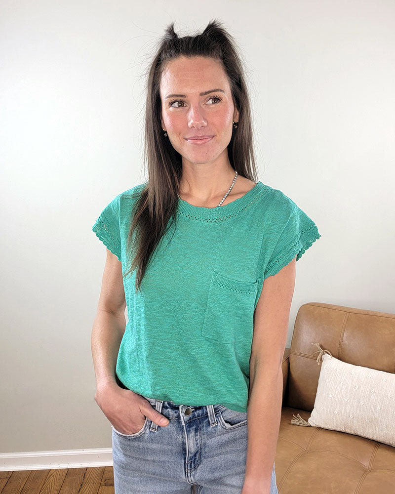 A woman with long brown hair models the Skye Short Sleeve Sweater by Staccato, paired with light blue jeans, standing indoors near a tan couch—a smiling look ideal for a transitional wardrobe.