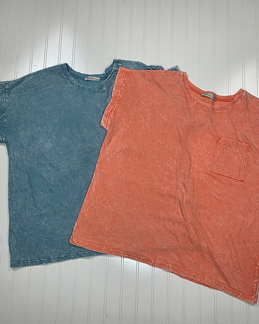 Two Jessie Crinkle Washed Rolled Short Sleeve Tops by ZENANA in 100% cotton, laid flat on a white surface. One is blue, the other orange with a chest pocket. Both feature relaxed fits, rolled sleeves, and visible seam details.