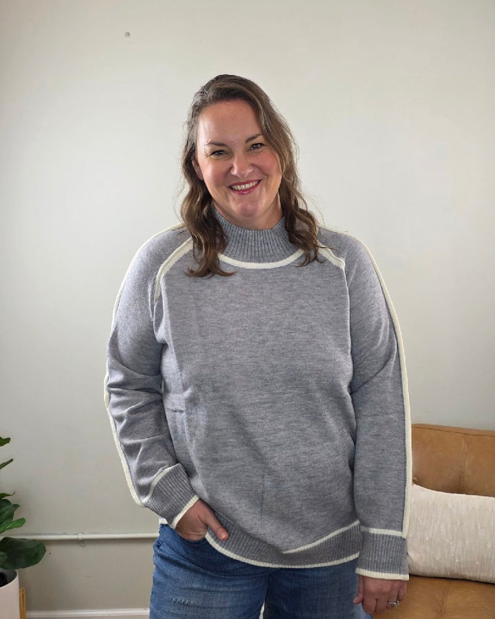 A woman wearing a grey Lime N Chili, Inc Kathy Sweater with white trim along the raglan sleeves and hem.