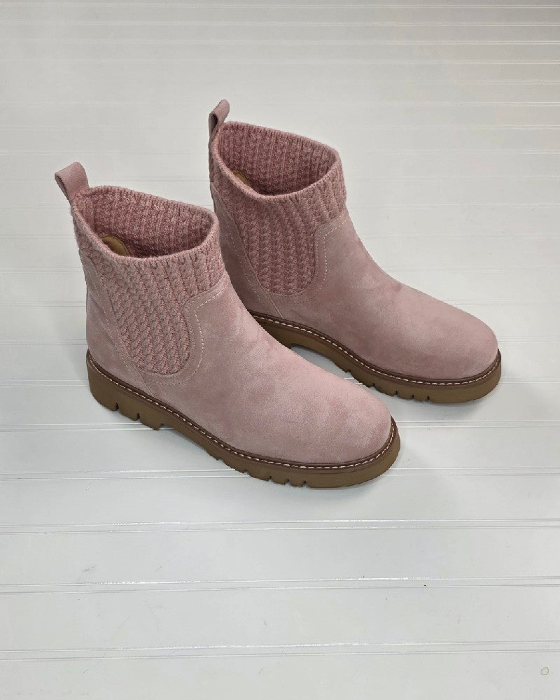 A pair of Corkys Keep Me Warm Boot by Corkys in pink, with a cable knit upper and a cozy suede-like finish, are elegantly displayed on a white wooden surface.
